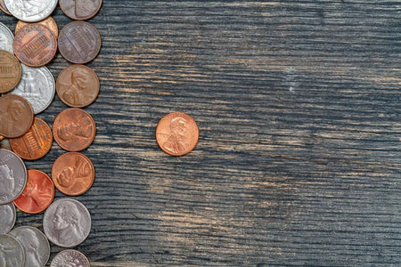 A pile of various coins on a dark wooden surface with one coin separated from the rest