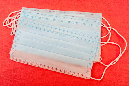 A light blue surgical face mask with white ear loops on a red backgroundの写真素材
