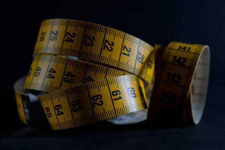 A yellow flexible measuring tape curled up on a dark surface, showcasing its measurement markings.