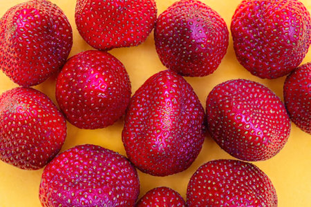 A close-up of several fresh strawberries on a yellow surface, showcasing their vibrant red color and textured surface.の写真素材