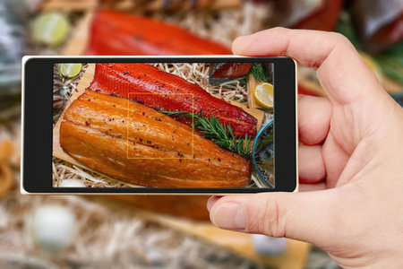 A hand holding a smartphone capturing a photo of a delicious dish with a large piece of meat and red...