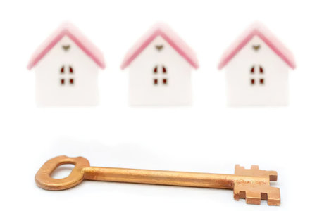 An image of a golden key in front of three small white houses with pink roofs.の写真素材
