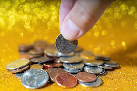A hand adding a coin to a pile of various coins on a gold surface