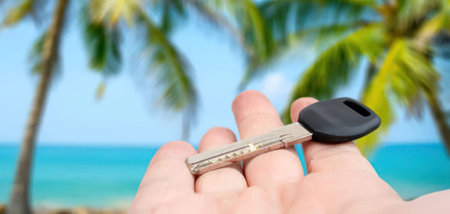 A hand holding a key with a tropical beach background, featuring palm trees and a vibrant ocean.の写真素材