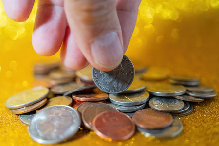 A hand holding a coin over a pile of various coins on a yellow surface