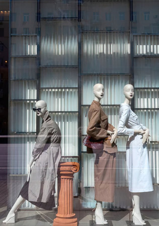 Three mannequins dressed in modern clothing are displayed in a store window, with a decorative...