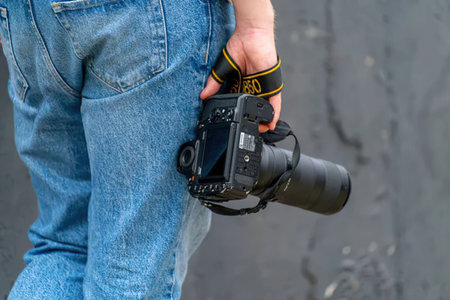 A person wearing blue jeans holding a black camera with a lens.