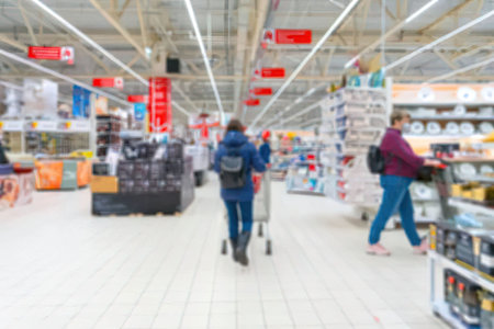The image shows a blurry view of people shopping in a supermarket aisle with shelves stocked with...