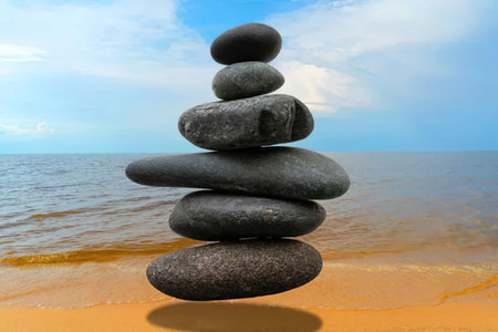 A stack of smooth stones on a serene beach with calm water and a blue sky.