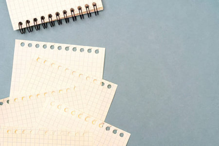 A spiral bound notebook with several pages fanned out on a blue surface