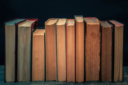 A collection of old books with worn covers and yellowed pages stacked horizontally on a shelf...