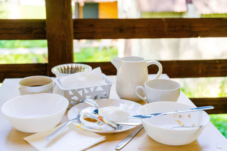 A table set with various white ceramic dishes and utensils on a white tablecloth, with a wooden...