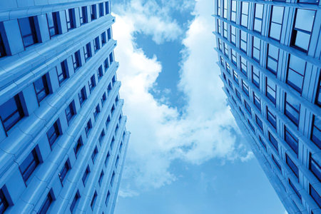 A low-angle shot of two tall buildings with many windows, set against a backdrop of blue sky and...