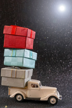 A vintage beige truck model with a stack of wrapped gifts in red, blue, and beige on its bed, set against a dark background with a bright light source.の写真素材