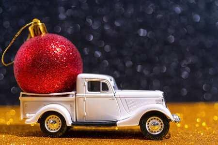 A small white vintage truck model with a large red glittery Christmas ornament in its bed, set...