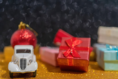A vintage toy car is parked next to several wrapped gifts on a gold glittery surface.