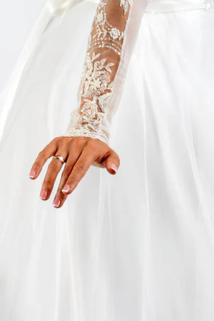 A close-up shot of a woman's hand and arm in a white wedding dress with a lace sleeve, showcasing her wedding ring.の写真素材