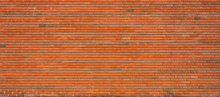 Red brick wall with varied shades of red and brown tones, featuring uneven bricks and mortar in a...