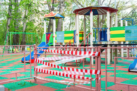 Colorful playground equipment is fenced off with red and white striped safety tape restricting...