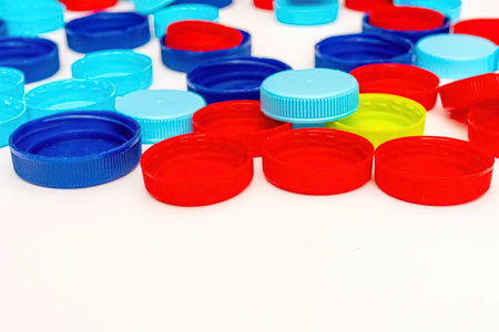 Multicolored plastic bottle caps are scattered randomly on a white background, showcasing a variety...