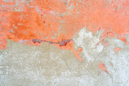 Distressed concrete wall with peeling orange paint reveals gray surface texture underneath, creating a rough and worn appearance.の写真素材