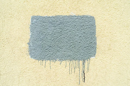 Gray rectangular paint smear with visible drips on a textured beige wall surface creates a unique...