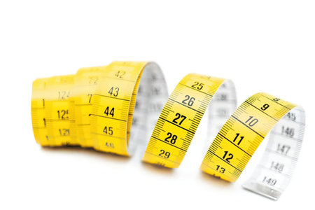 Three flexible yellow measuring tapes with black numbers curled and standing upright on a white...