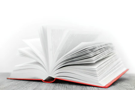 Open red book lies on a wooden surface with its pages fanned out, showcasing its contents against a...