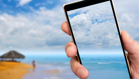 Person captures a serene beach scene on their smartphone screen with a blurred tropical landscape...