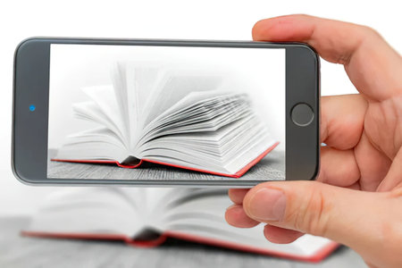Person holding a smartphone taking a photo of an open red book lying on a gray wooden table.