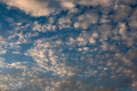 Beautiful blue sky filled with small white cumulus clouds on a sunny day symbolizing serene and...
