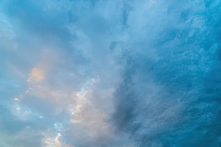 Soft blue sky filled with fluffy white clouds and subtle pink undertones, creating a serene atmosphere during a peaceful sunrise or sunset.の写真素材