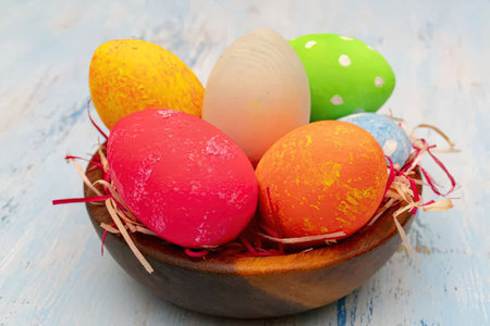 Colorful easter eggs beautifully arranged in a wooden bowl with festive decoration on a whitewashed...