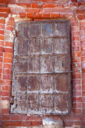 Old metal door is embedded in a red brick wall showing signs of rust, aging, and wear.