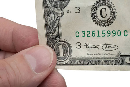 A hand holds a one dollar bill with a close-up view of the currency showcasing intricate details and...