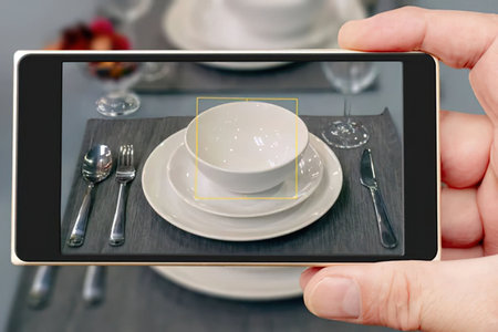 Person holds a tablet displaying a formal table setting with white dinnerware and silverware on a...