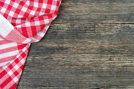 Red checkered kitchen cloth draped over rustic wooden surface showing texture and pattern of fabric...