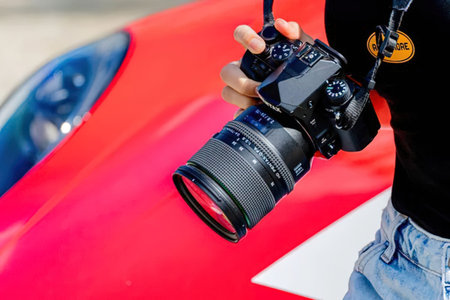 Photographer in black shirt and jeans holding a professional camera with a large lens standing next...