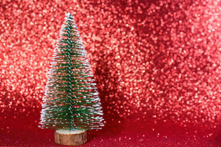 Small green christmas tree on a wooden base against a vibrant red sparkling background, creating a...