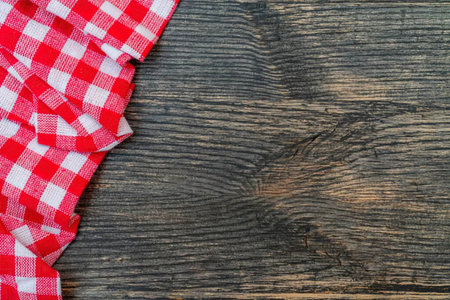 Red and white checkered tablecloth draped over edge of rustic dark wooden table with visible wood...