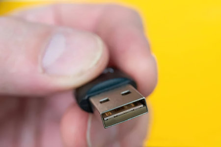 A hand grasps a USB connector against a vibrant yellow background, symbolizing data transfer and...
