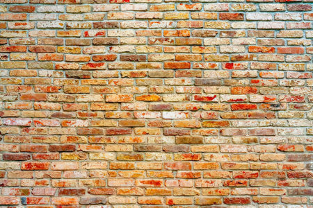Weathered brick wall featuring shades of red, orange and yellow bricks in various conditions and...
