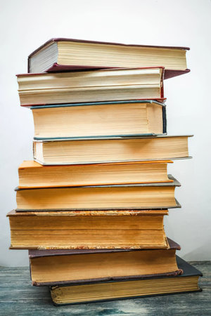 Stack of old hardcover books on a wooden table against a plain white background, representing...
