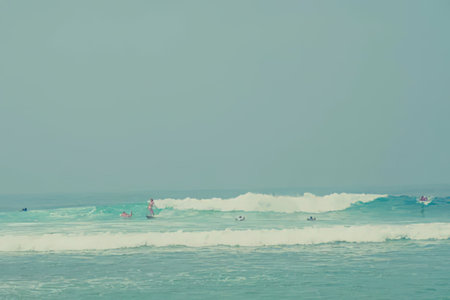 Surfers ride a gentle wave on a calm ocean blue day with clear skies everywhere, enjoying a peaceful...
