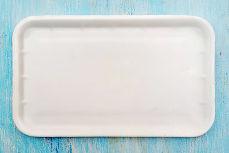 White disposable rectangular styrofoam plate on a light blue painted wooden background surface ready...