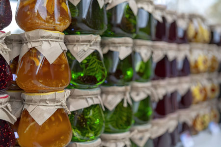 Glass jars filled with colorful homemade preserves are neatly displayed on a wooden shelf with...