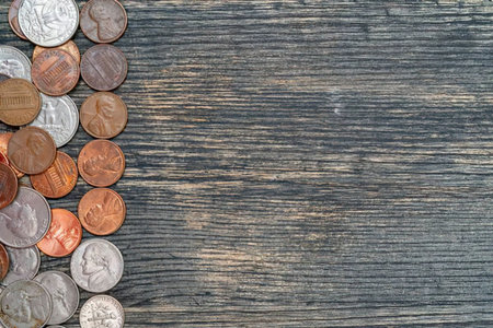 Various denominations of coins scattered on a dark wooden texture symbolizing savings and financial...