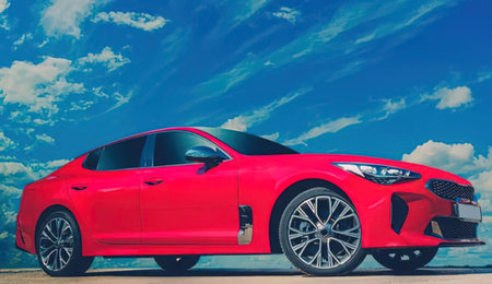 Bright red modern car parked on a roadside against a bright blue sky with white clouds, showcasing...