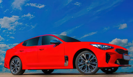 Modern red sports car parked on a flat surface against a blue cloudy sky background showcasing its sleek exterior and vibrant red color.の写真素材