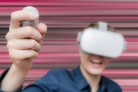 Man excitedly plays with a virtual reality headset and controller in front of a red background,...